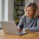 Frau am Kuechentisch prueft skeptisch eine E-Mail am Laptop
